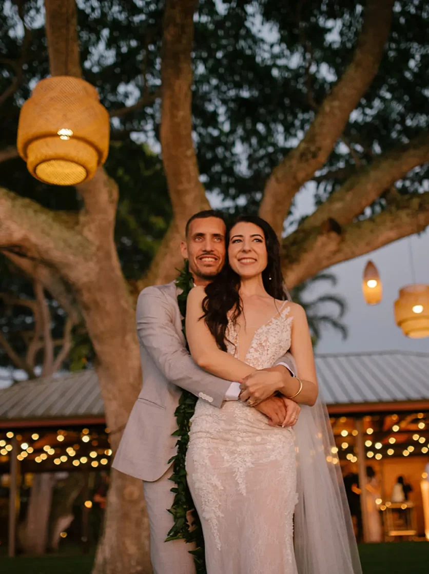 Bride and groom under tree adorned with string lights at Holualoa Inn near Kona