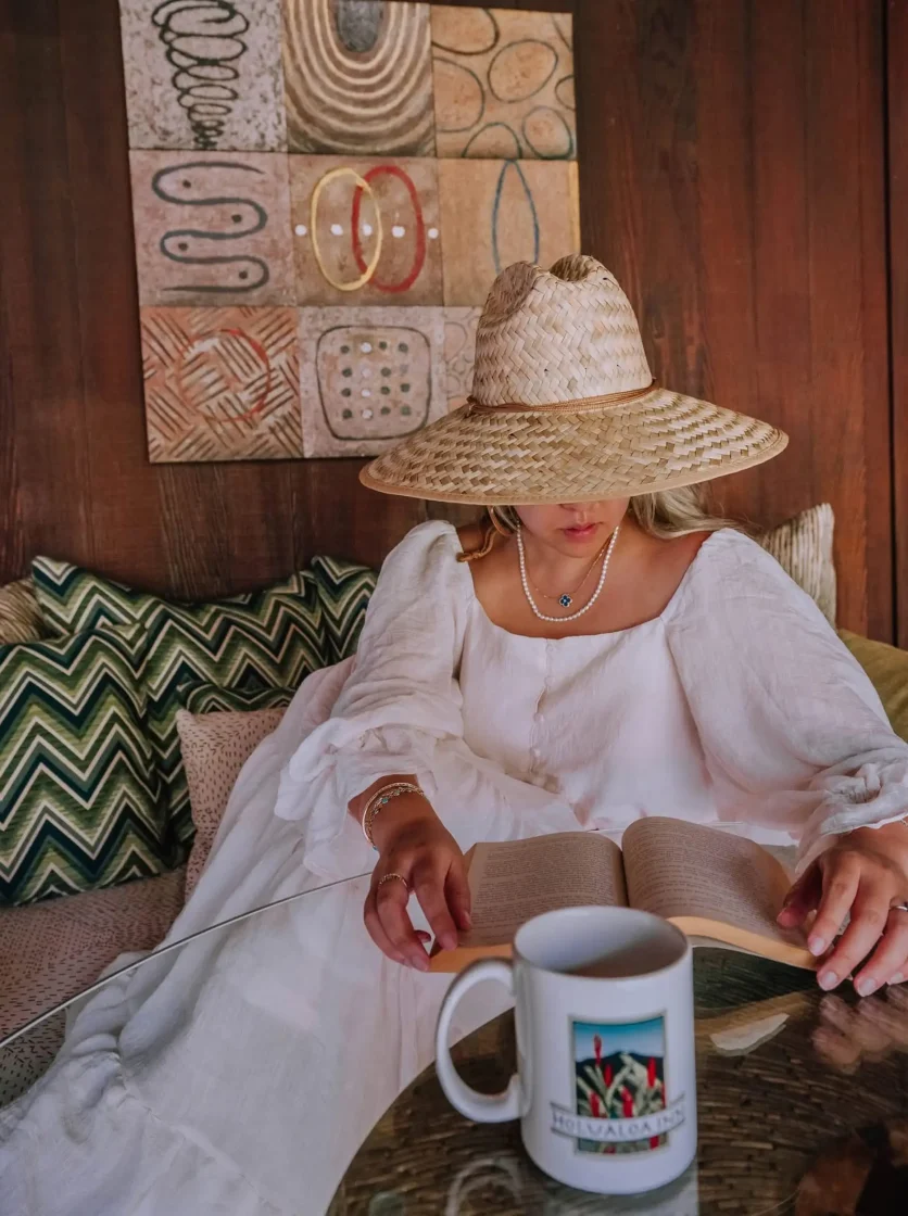 Woman in sun hat relaxing with coffee and book indoors
