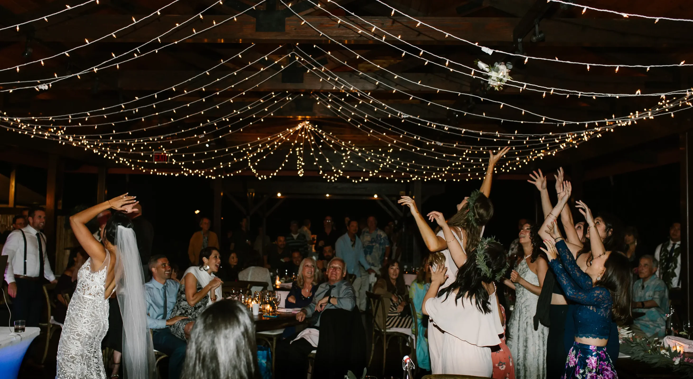 Bride throwing her bouquet under pavilion with string lights